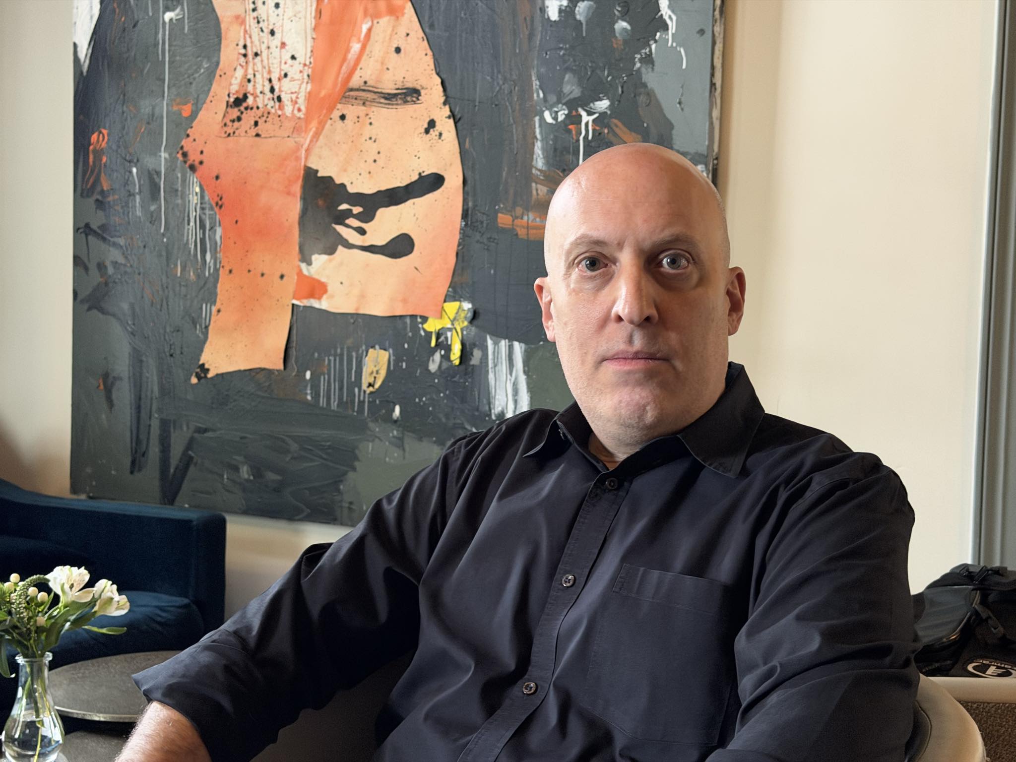 Portrait of Houston artist Howard Sherman seated in front of one of his paintings at La Colombe d’Or