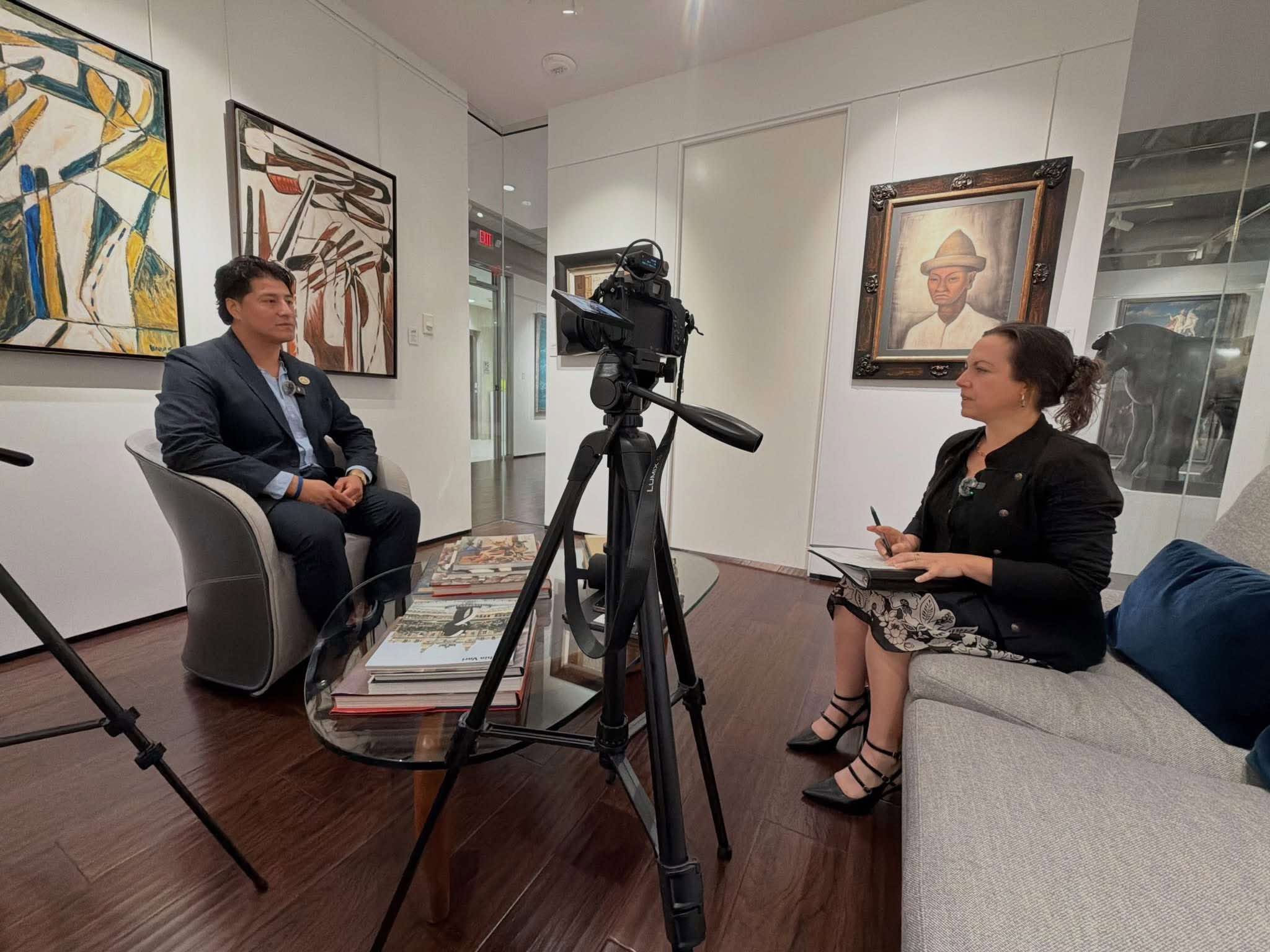 Ronaldo Salgado and Lisbet Newton seated for an interview, with a camera on a tripod between them.