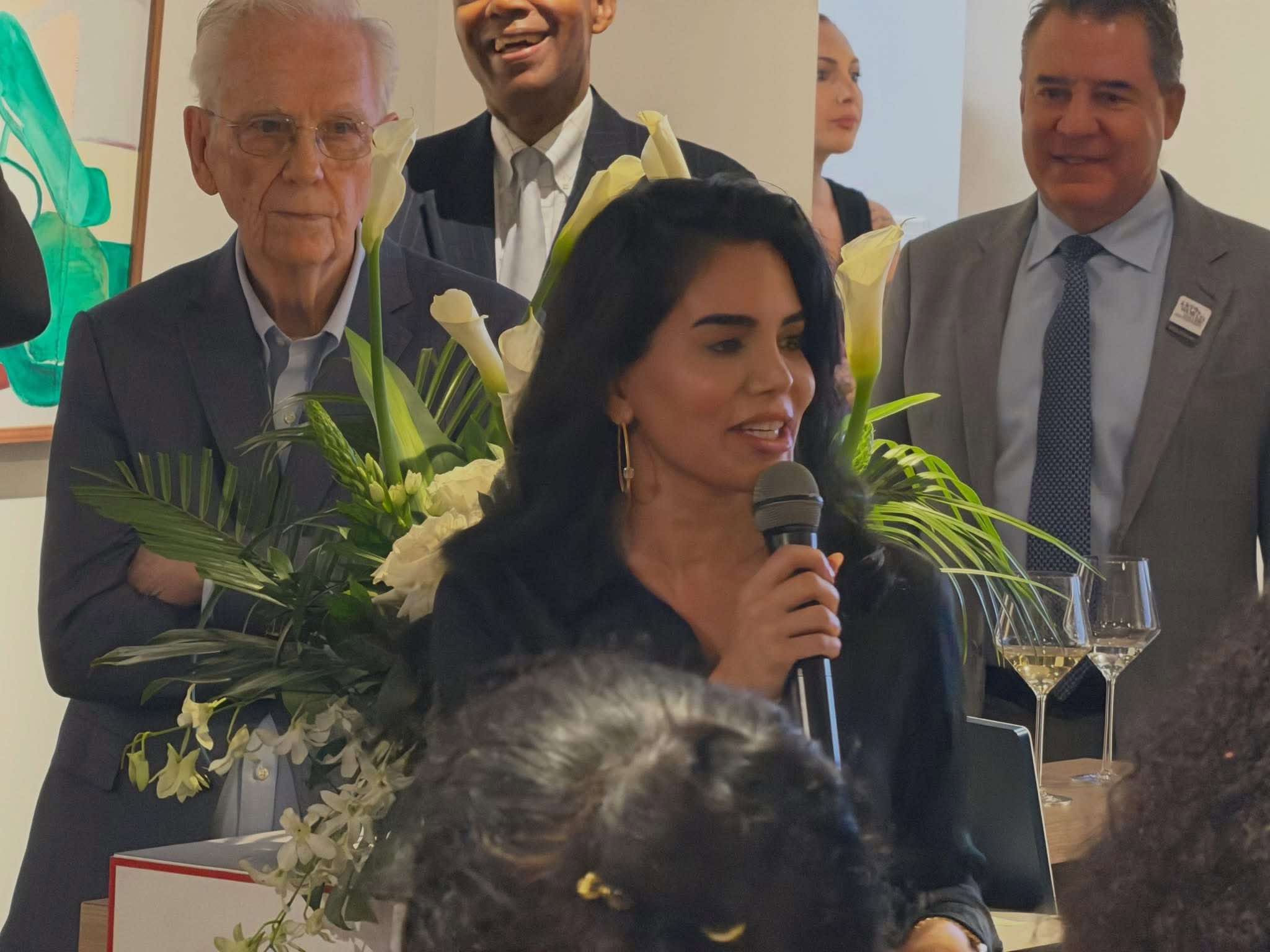 Nina Magon holding a microphone while speaking during the Arrival Awards kickoff program.