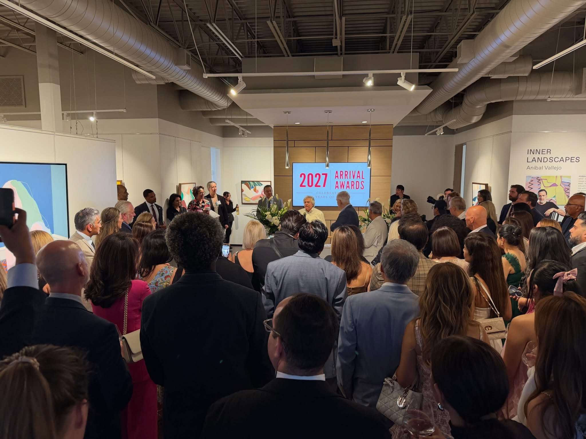 Guests gathered for remarks beneath a screen displaying the 2027 Arrival Awards at Art of the World Gallery.